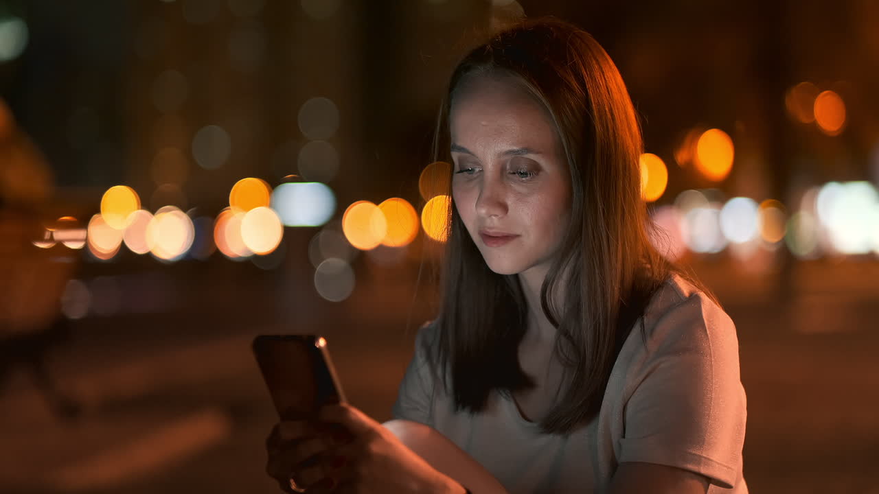 Young woman tourist travels through the night megalopolis and writes text messages on social networks about the journey holds the phone in her hands and looks at the screen of the gadget