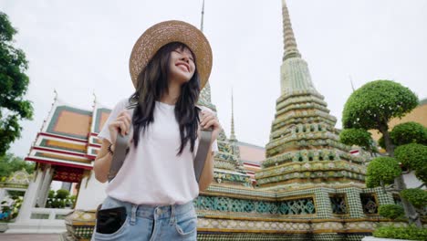 cheerful young asian woman traveling at wat pho temple in bangkok, thailand.