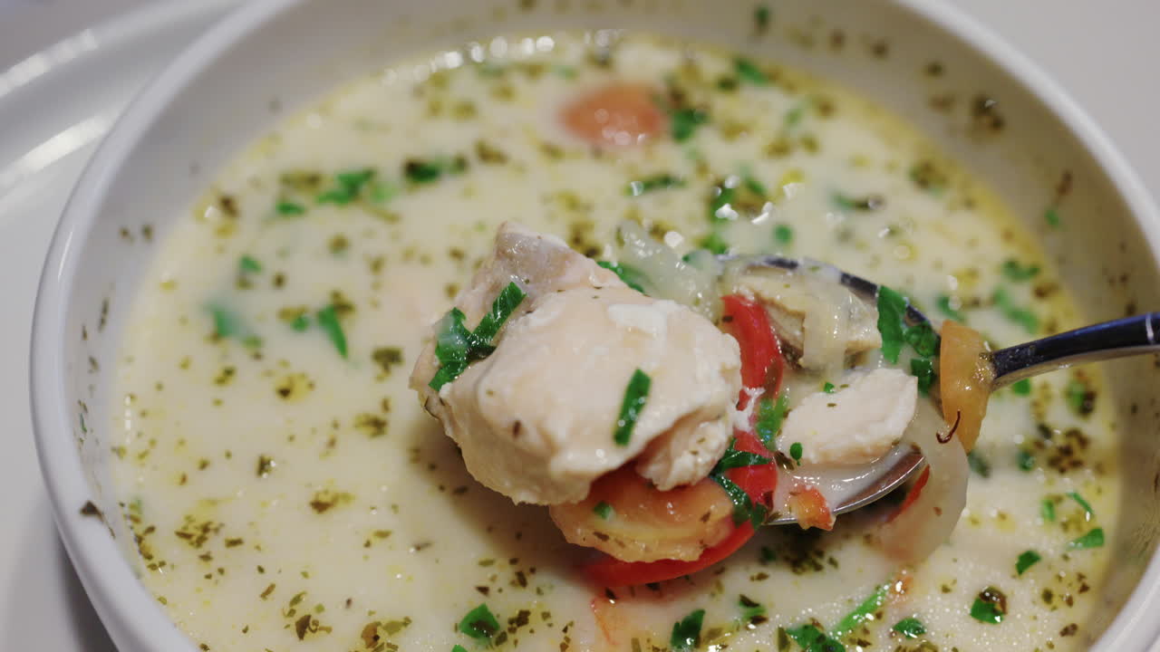 Primer plano de sopa cremosa de salmón con hierbas y verduras siendo removida con una cuchara
