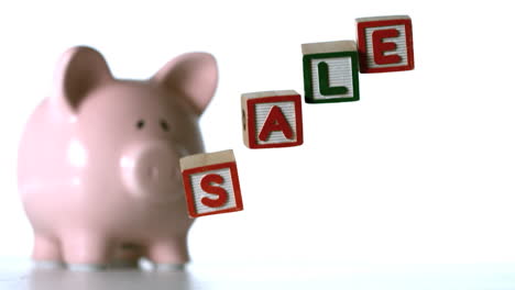 alphabet blocks spelling sale falling over in front of a piggy bank