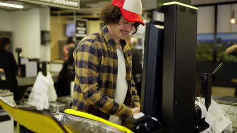 happy food delivery guy in a plaid shirt punches the necessary products and then puts them in his yellow bag for food delivery in the supermarket