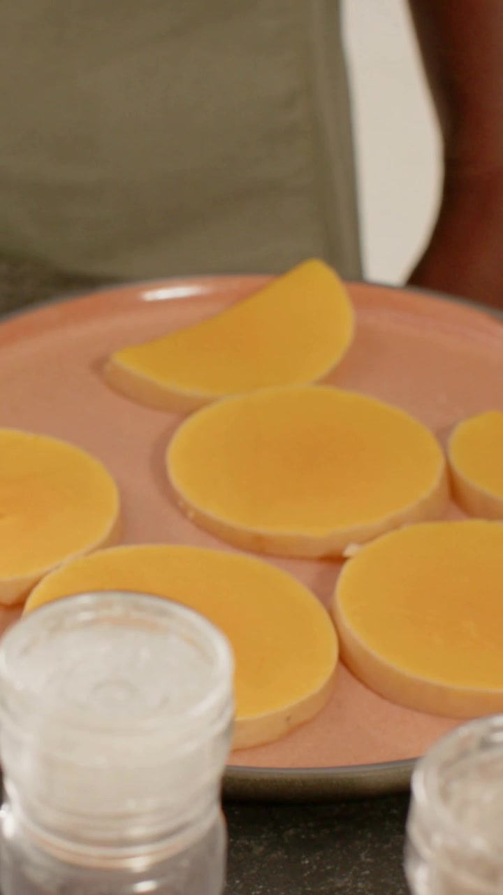 Vertical video: Scooping spoon from left, green-apron man stacking discs on pink dish at counter
