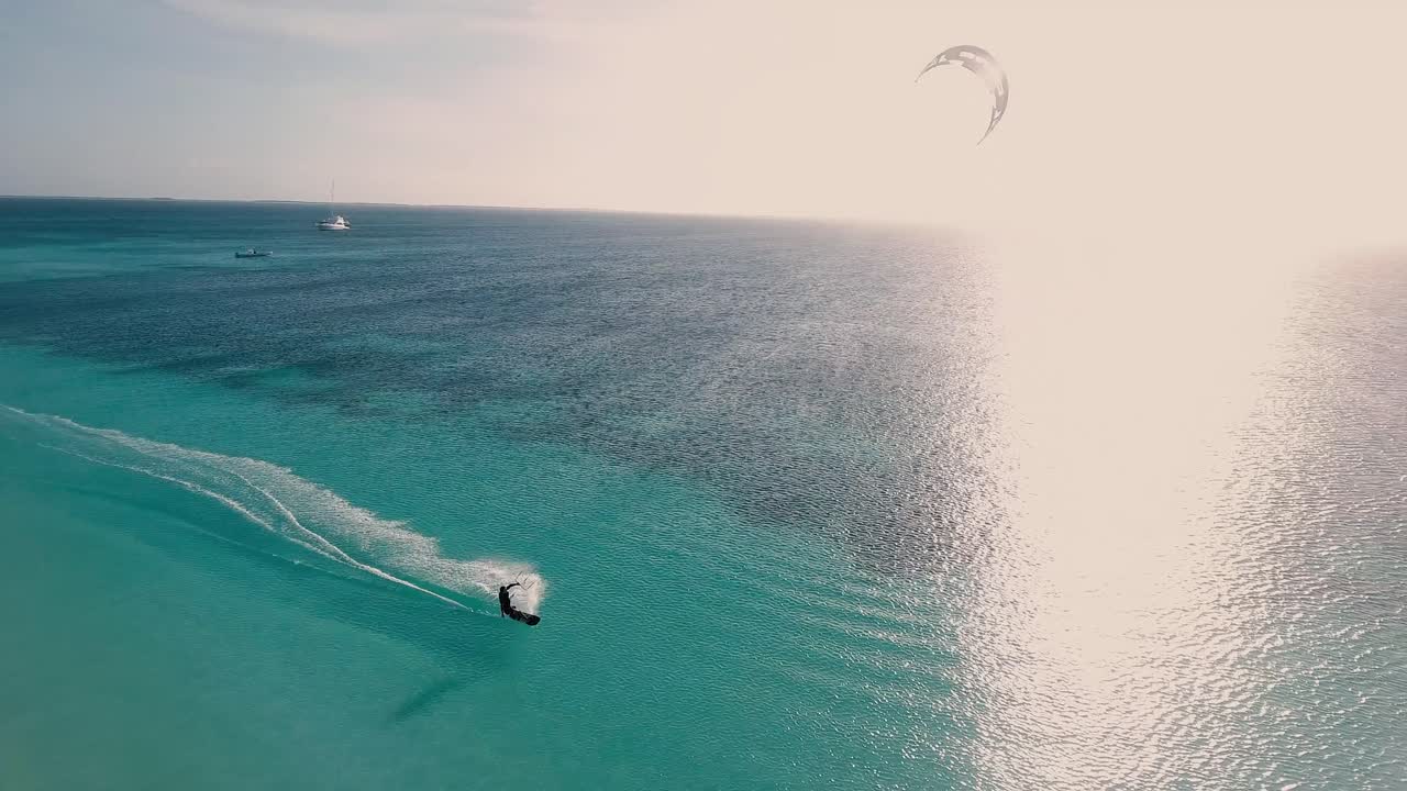 hombre kitesurf retroiluminado al atardecer en agua de mar turquesa, drone shot pan right los roques