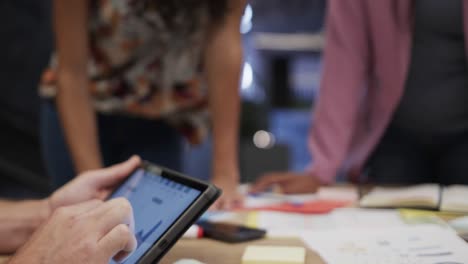 mid section of diverse male and female colleagues in discussion using tablet in office, slow motion