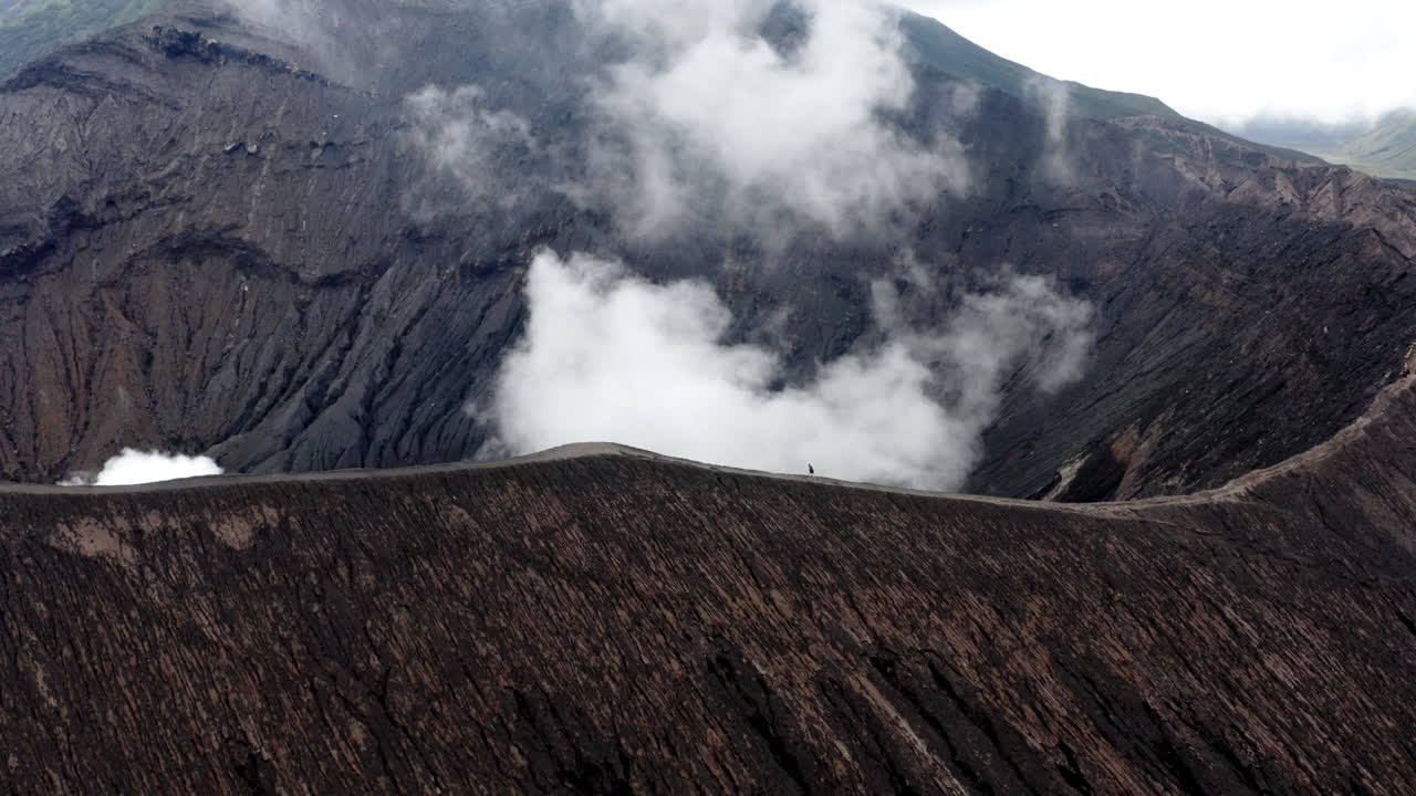 Active Mt Bromo Volcano, Aerial orbit shot as traveler hiking peak