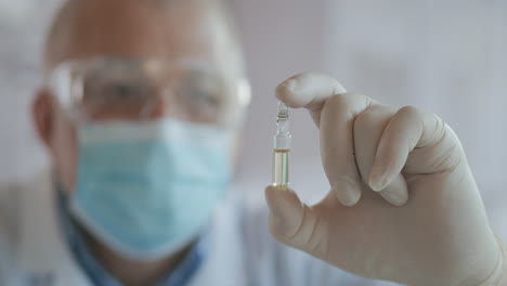 primer plano del desarrollador de la vacuna contra el coronavirus sosteniendo una ampolla de líquido blanco examinando y sosteniendo la vacuna en guantes. imágenes de alta calidad 4k