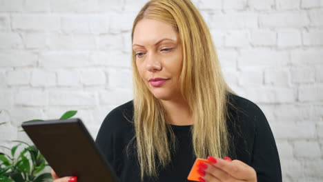 A-blonde-woman-using-a-credit-or-debit-bank-card-to-pay-for-shopping-online-using-a-tablet