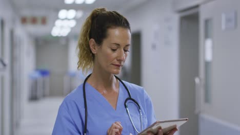 Thougtful-caucasian-female-health-worker-using-digital-tablet-in-the-corridor-at-hospital