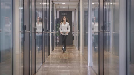 Businesswoman-Riding-Along-Corridor-In-Modern-Office-On-Scooter