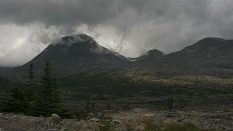 huge alaskan mountains loom in the distance as clouds rest at their peaks