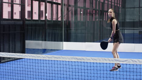 young woman playing padel tennis on indoor court, focused and ready to hit