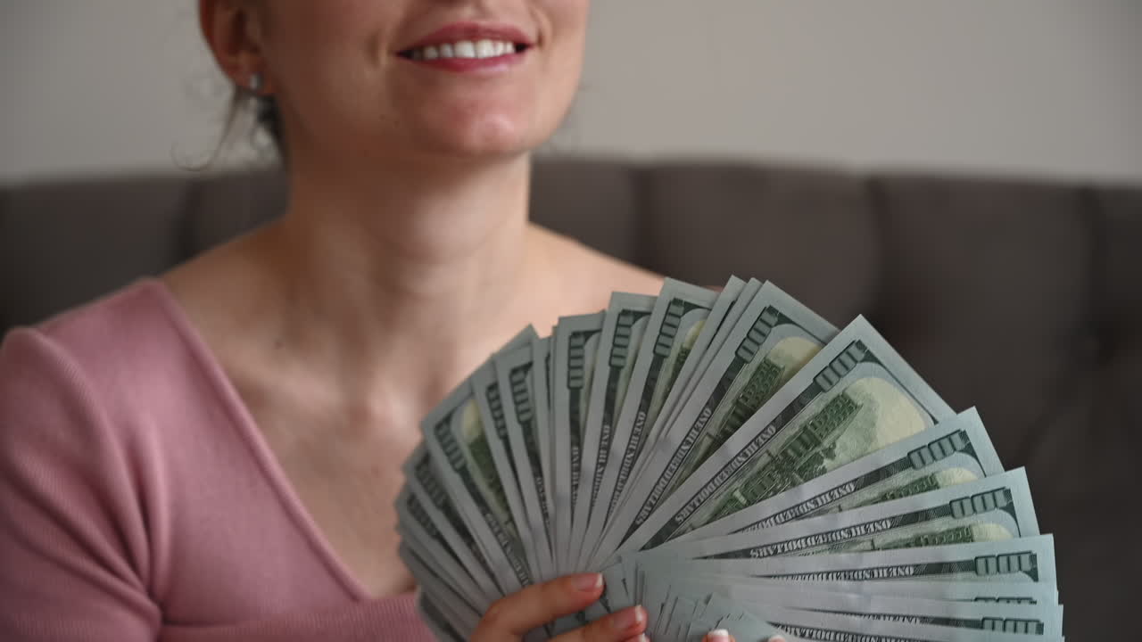 Smiling woman admiring a large fan of one hundred dollar bills in her hands