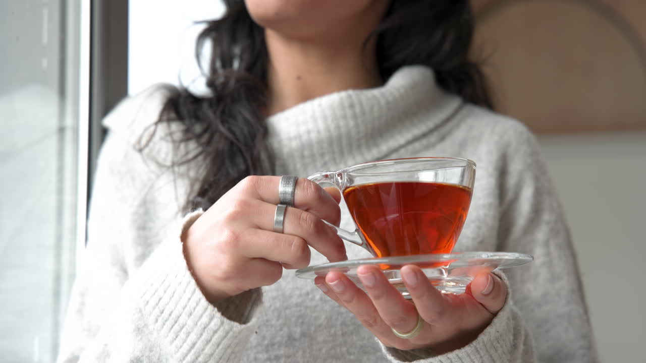 Woman enjoying warm tea in cozy sweater by window at home
