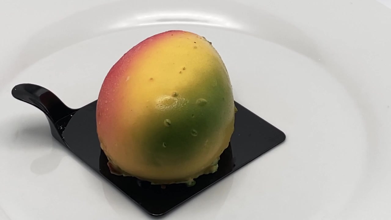 Dessert realistico a forma di mango, pasticcino trompe l'oeil su espositore rotante, isolato su sfondo bianco