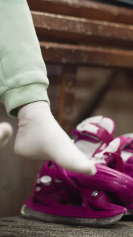 una vista de cerca de alguien sentado en un banco, con calcetines blancos y pantalones verdes, con patines de hielo rosados y un zapato negro al lado, la persona juega colgando sus piernas