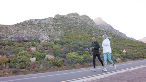 Happy-senior-biracial-couple-running-on-road-in-mountains