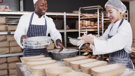 hombre y mujer panaderos felices trabajando en la cocina de la panadería, vertiendo harina en el pan, en cámara lenta