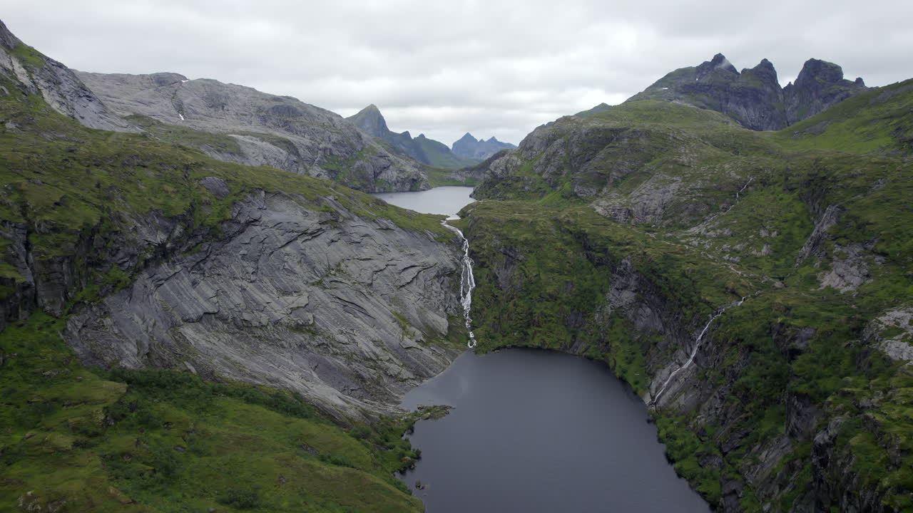 Ripresa aerea con dolly in avanti di una cascata spettacolare tra le montagne con scogliere rocciose a Trolldalsvatnet, Lofoten, Norvegia.