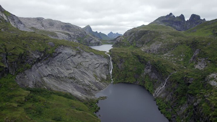 Ripresa aerea con dolly in avanti di una cascata spettacolare tra le montagne con scogliere rocciose a Trolldalsvatnet, Lofoten, Norvegia.