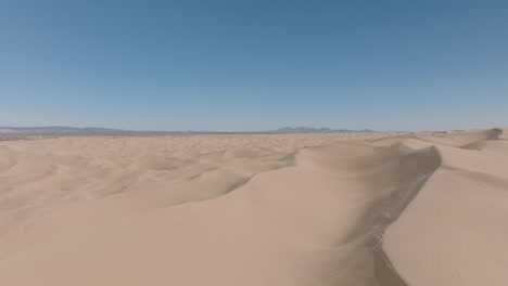 Toma-Panorámica-Con-Drones-De-Dunas-Arenosas-Del-Desierto-En-El-Desierto-Del-Sudoeste-De-California,-Cielos-Azules-Por-Delante