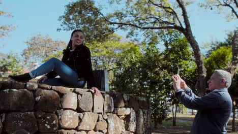man taking a picture of a woman posing on a stone wall outdoors