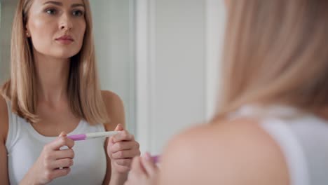 mujer joven de pie frente al espejo del baño y esperando los resultados de la prueba de embarazo.
