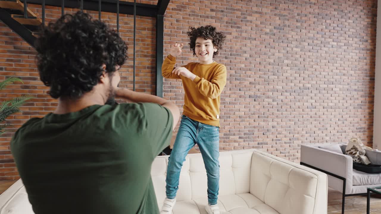 Biracial boy dances on sofa having fun with elder brother