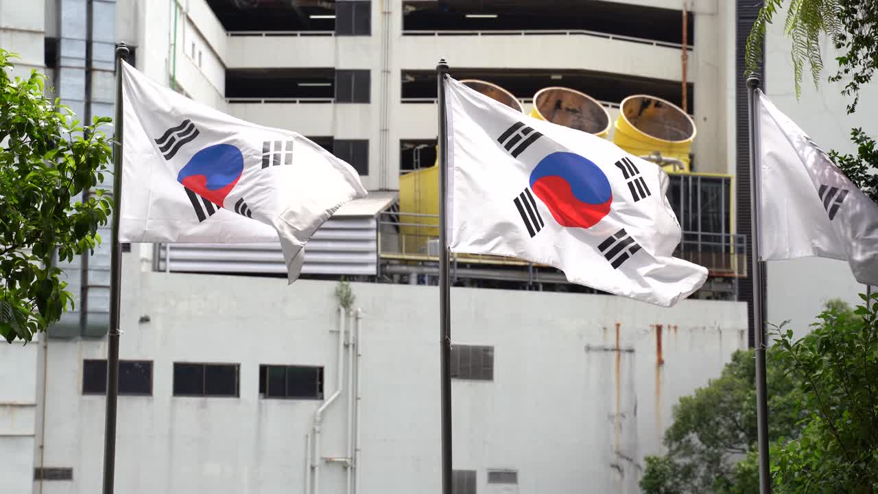 tres banderas de corea del sur ondeando con edificios en el fondo en un día ventoso