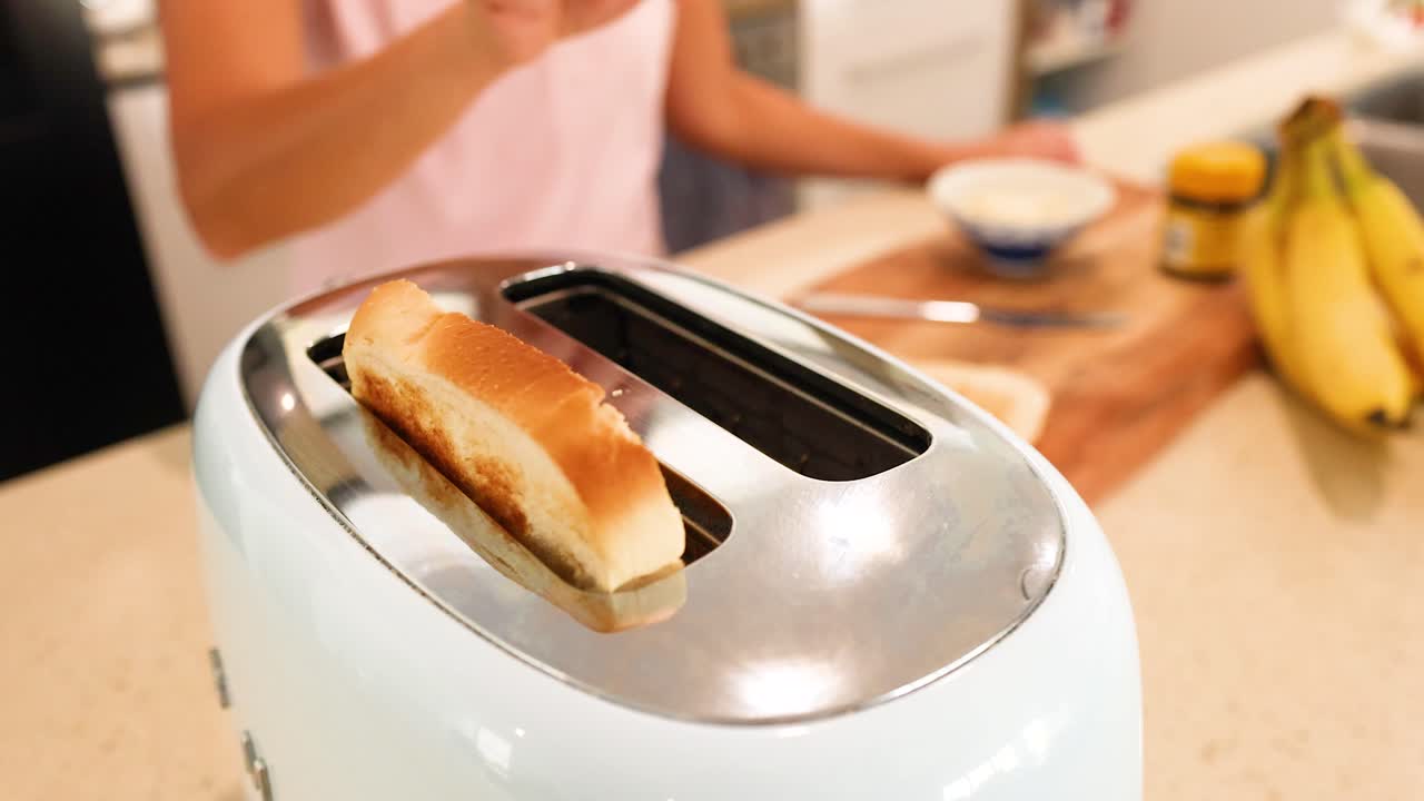 A person toasts bread in a bright kitchen, capturing the process from insertion to removal