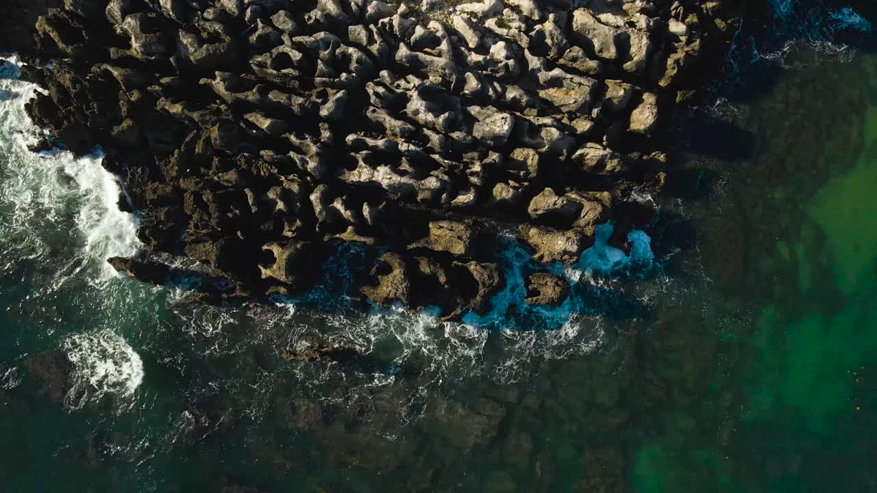 Video aereo dall'alto con drone di scogliere e rocce taglienti, alte e pericolose sulla costa del Portogallo, dove le onde spumeggianti di acqua di mare colpiscono la roccia con grande forza, creando schiuma e bolle