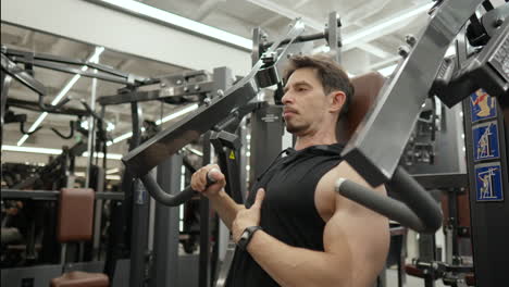 Hombre-Musculoso-De-40-Años-Haciendo-Prensa-De-Pecho-Sentado-Con-Una-Mano-En-El-Gimnasio