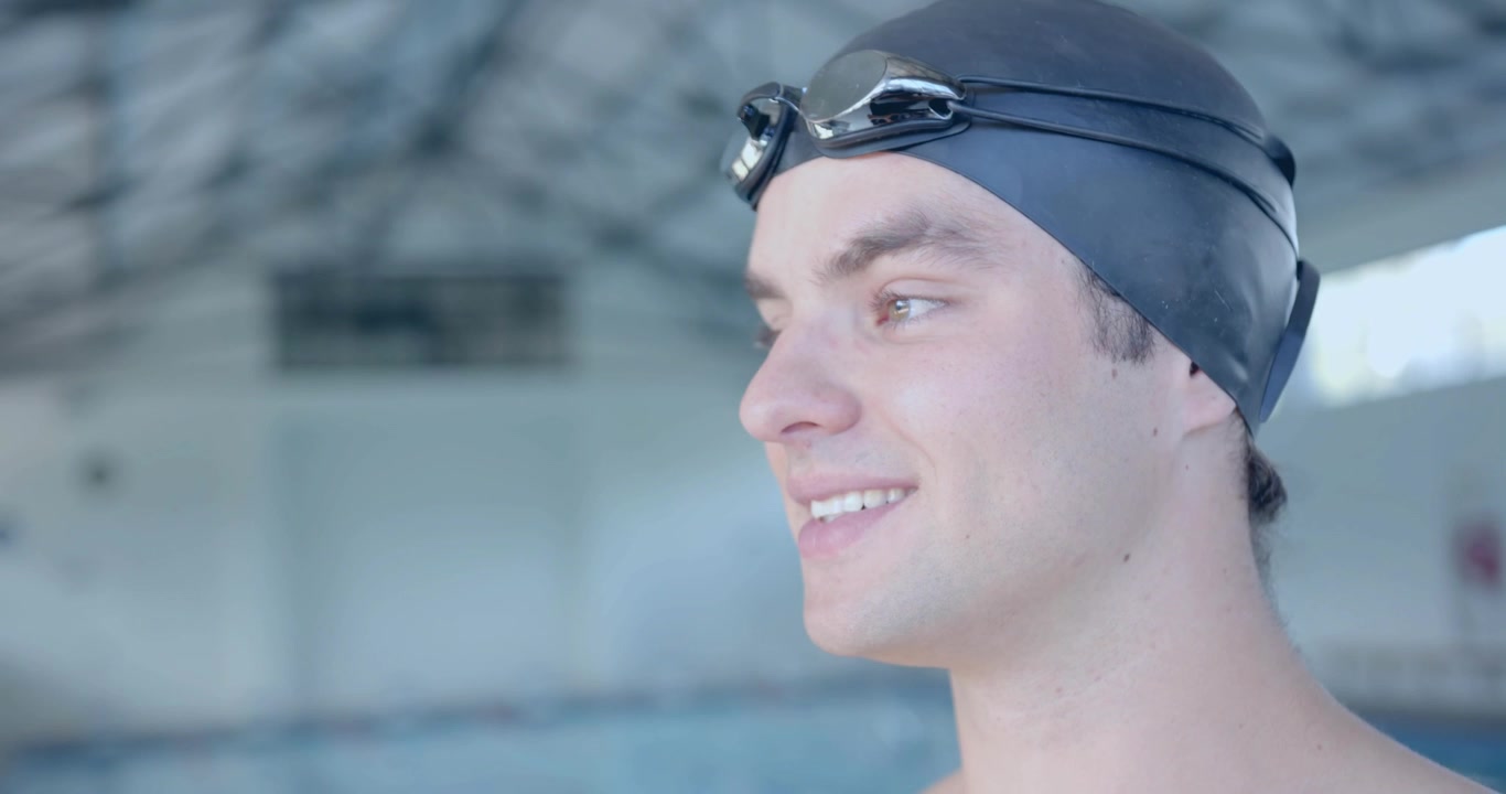 Ein männlicher Schwimmer blickt auf die Bahnen, dreht den Kopf während des Sporttrainings, lächelt und passt seine Schwimmbrille an.