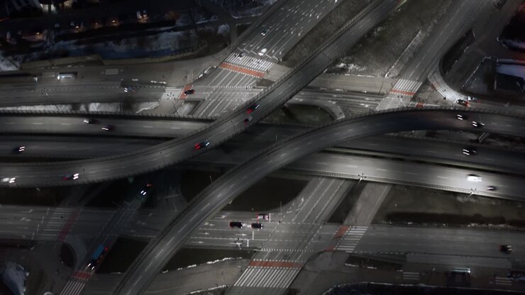 Aerial time lapse hyperlapse traffic jam interchange road at night, drone shot top view roadway intersection in city in evening. Timelapse cars driving busy junction highway in fast motion