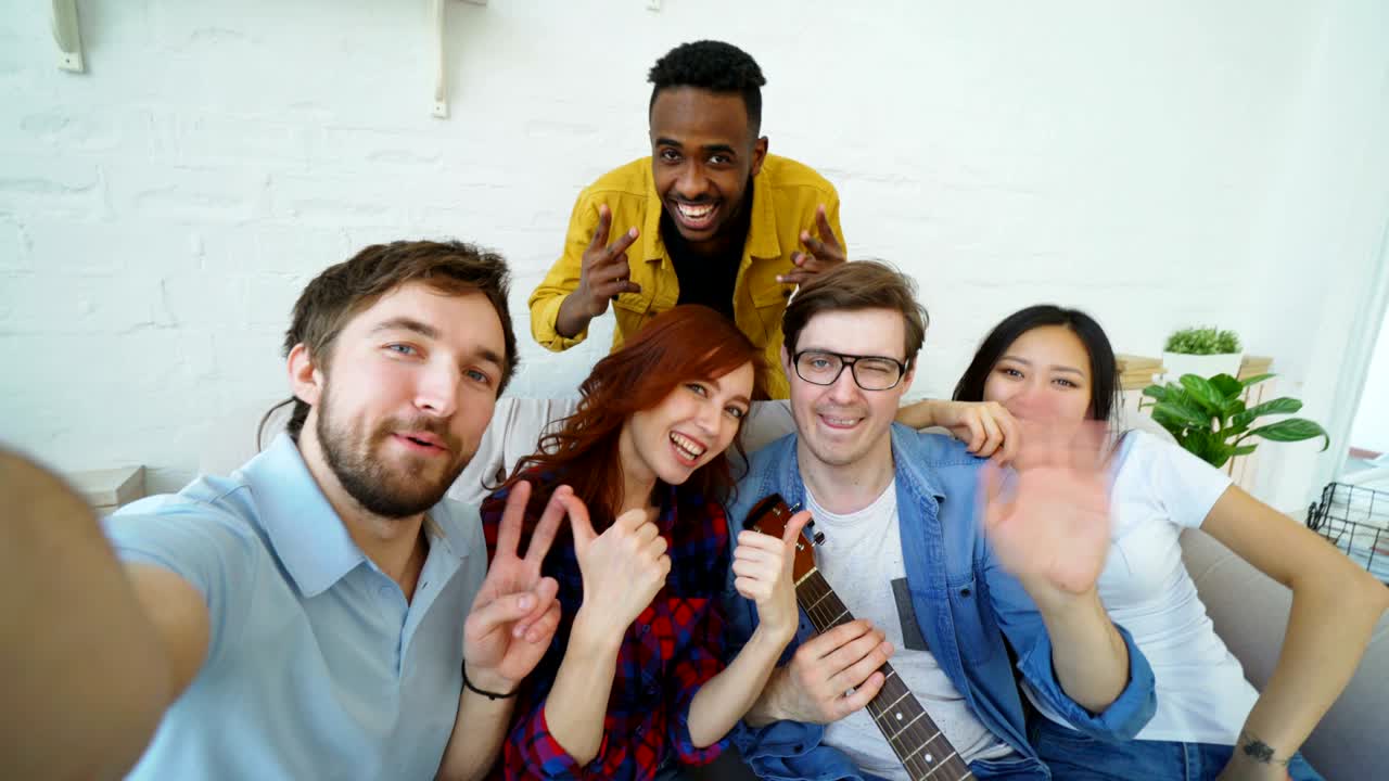 집 안의 파티에서 축하하는 동안 스마트폰 카메라로 셀피 사진을 찍는 여러 민족의 쾌활한 친구들의 포인트