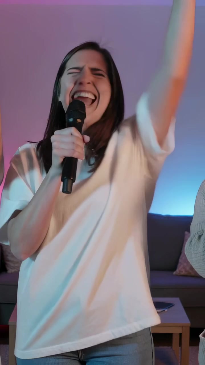 Vertical video: Singing woman inhaling and pulling mic closer at home karaoke wearing tee and jeans