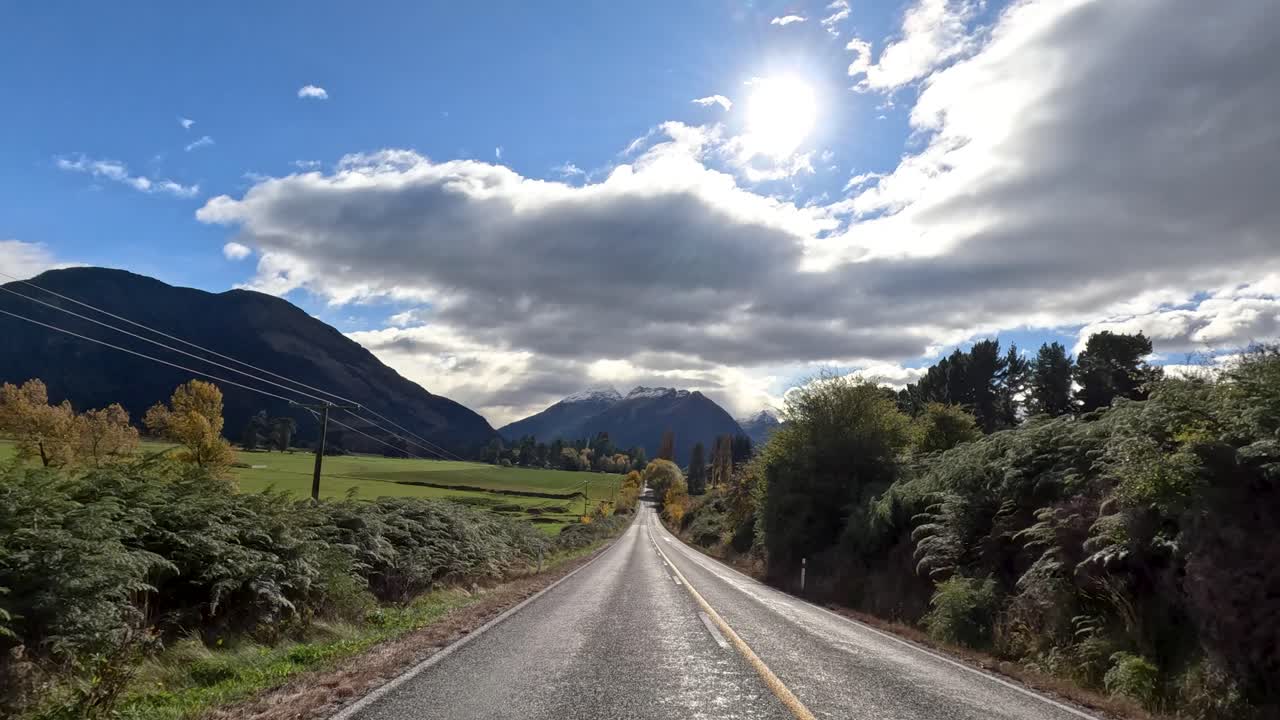 Forward-facing camera captures sunny rural road, mountains, and lush greenery under dynamic clouds