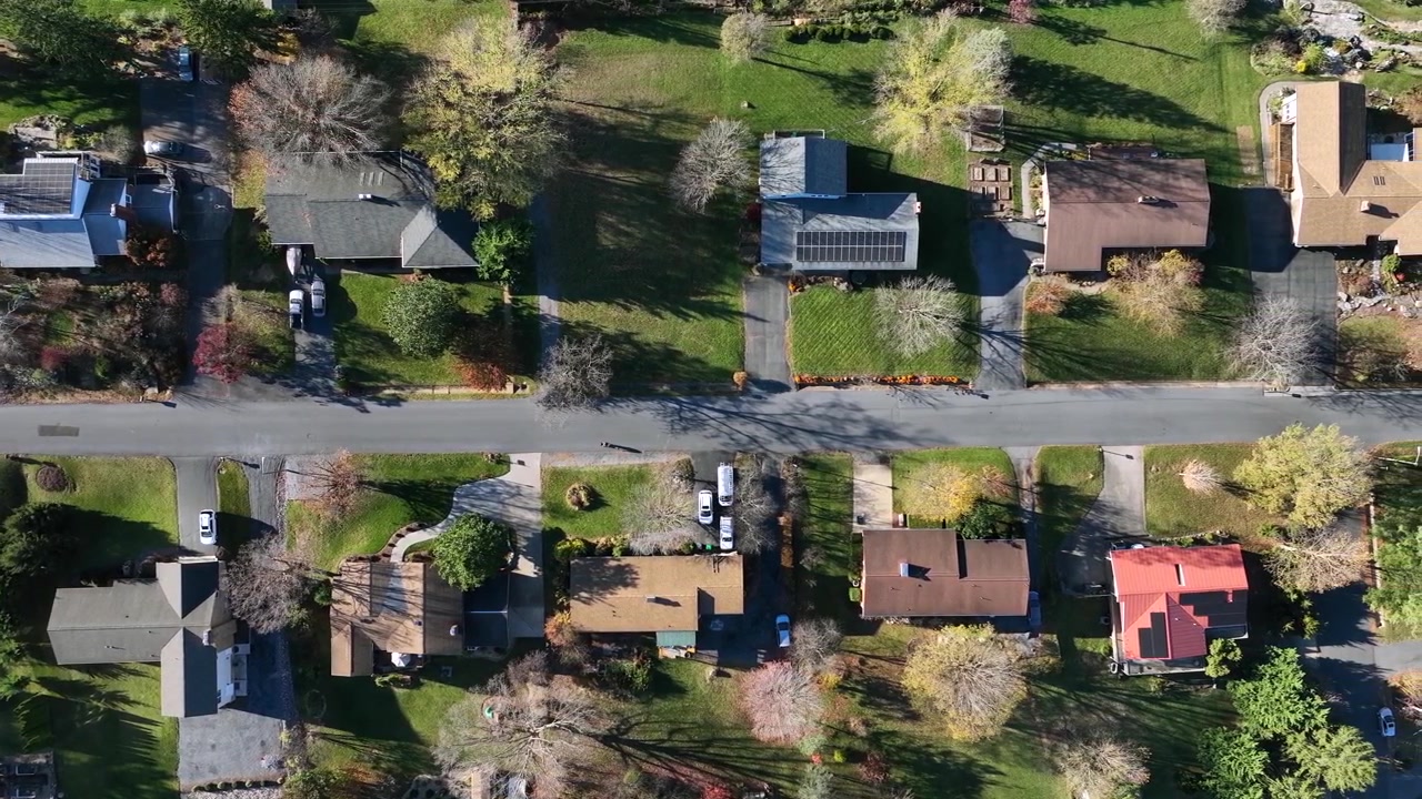 Rua reta com casas modernas de classe alta em um subúrbio americano. Painéis solares nos telhados de casas unifamiliares. Imagem aérea de cima para baixo. Estação de outono com árvores coloridas sob a luz do sol.