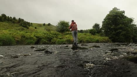 wide angle shot of a man flyfishing and wading in a river in scotland