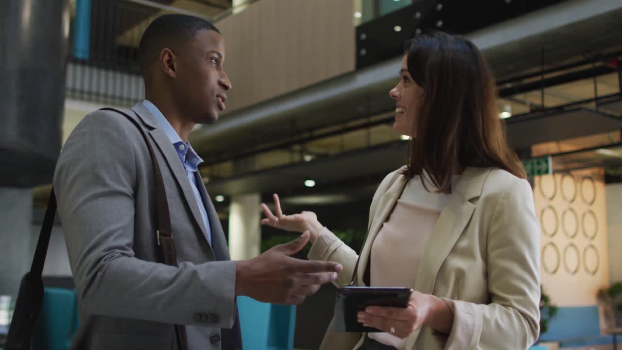 Diverse businessman and businesswoman talking and using tablet in lobby of modern office