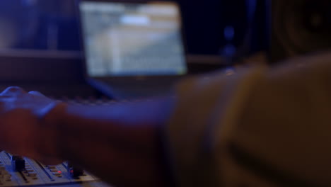 primer plano de las manos masculinas presionando los botones y girando hacia arriba y hacia abajo la placa de sonido o el mezclador en el estudio de sonido oscuro mientras se trabaja con una música