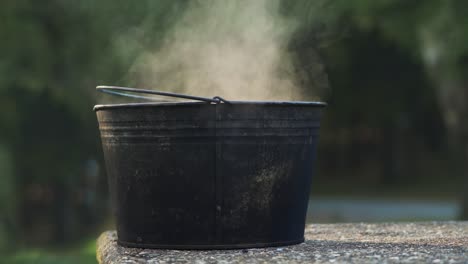 Dampfender-Wascheimer-Aus-Metall-Auf-Einem-Picknicktisch-Aus-Beton