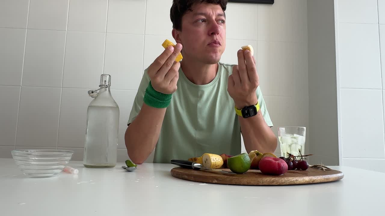 Uomo che mangia frutta fresca e beve acqua al tavolo della cucina.