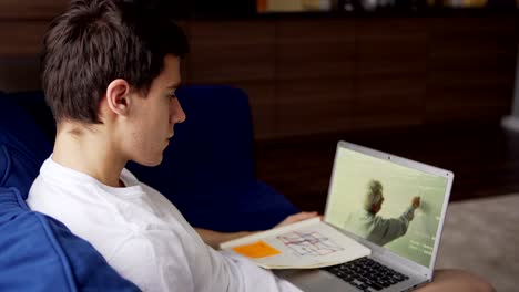 vista lateral inclinada de un estudiante universitario sentado en el sofá en casa y estudiando en línea viendo una lección de video con el maestro