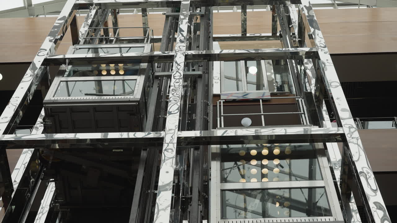 Modern glass elevators in motion, one ascending and one descending, surrounded by reflective metallic structure and architectural details