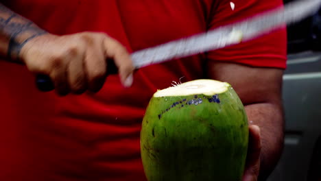 cámara lenta de la mano masculina con un cuchillo grande de machete cortando coco de una palmera bebiendo agua fresca y saludable