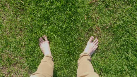 a point of view shot looking down at a white mans feet and toes standing on fresh green grass