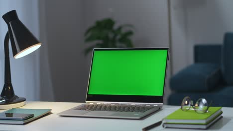portátil con pantalla verde en la mesa de trabajo en la oficina de casa, el hombre está encendiendo la mesa y las lámparas de piso en la sala de estar