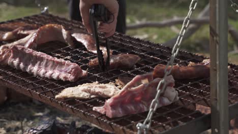 a dynamic handheld shot of grilling meat outdoors on a hanging grill