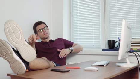 young lazy office worker in glasses relaxing in office with his legs on the table in the modern office throwing pieces of paper to the bin. shot in 4k