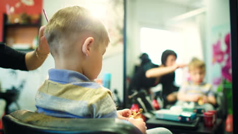 hairdresser cutting childs hair while he playing with a toy
